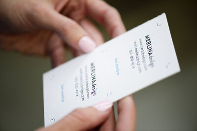 Branding image of a woman's hands holding a press printed business card for Merlina Design.