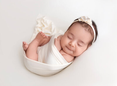 Newborn baby wrapped in white smiling at het photo session with Rochel Konik Photography