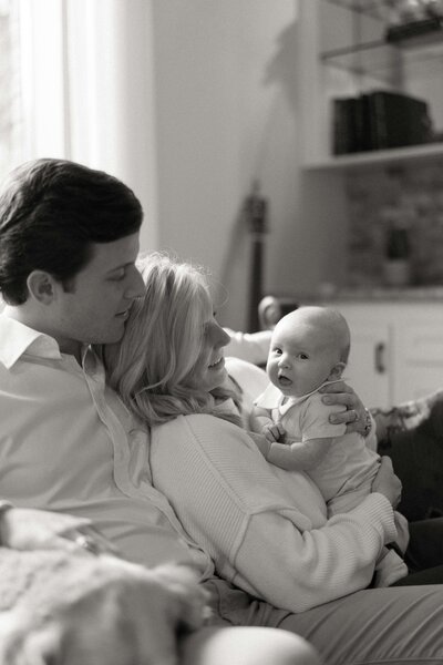 Black and white photo of mom and dad sitting together holding their newborn baby