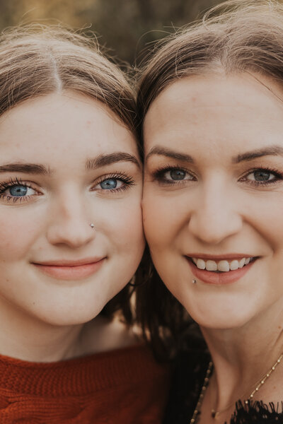 A mother and daughter are side-by-side, face-to-face, close to the camera, smiling