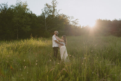 An couple expecting their first baby stand together facing each other in a grassy field during golden hour at Wing Deer Park in Johnson City, TN. Michaela Crawford Photography, a cinematic maternity photographer located in Northeast, TN. 