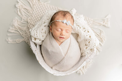 baby girl in white with blue bow on head sleeping in white basket