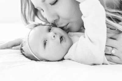 Mother kisses infant during Minneapolis newborn photoshoot.