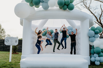 Corporate team bouncing in white bounce house with blue and green balloon garland