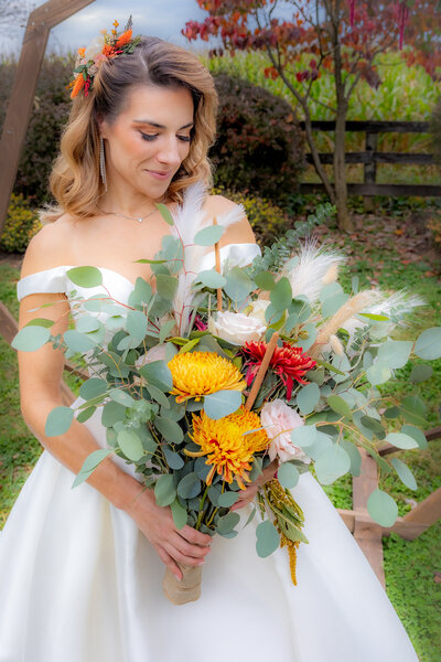 Bride holds a beautiful bouquet of flowers wearing a white off the shoulder wedding dress