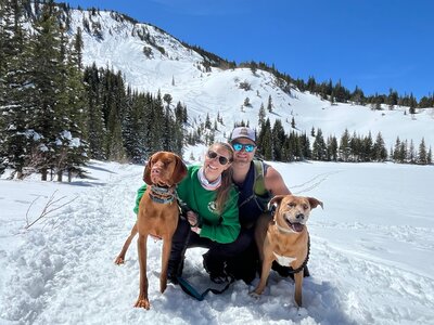 Therapist and girlfriend with their dogs in the snow on a mountain