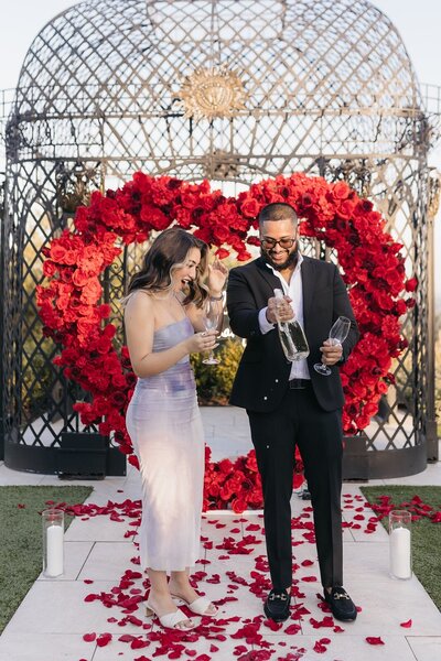 red heart arch with couple popping champagne Styled by Yours Truly, a wedding planner and designer in New Jersey.