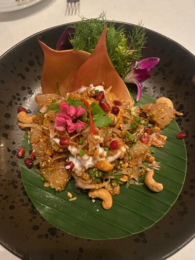 A gourmet dish served on a large leaf, featuring tropical fruits, herbs, and garnishes, part of a luxury dining experience.