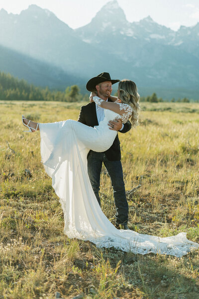 Grand Teton elopement photography by Adriana Montoya Photo. A groom wearing a cowboy hat holds his bride. They are looking at each other and the Grand Tetons are behind them.