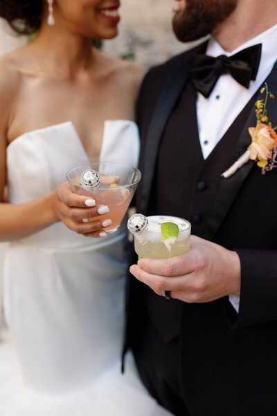 Bride and groom smile at each other while holding cocktails with disco ball stirrers.