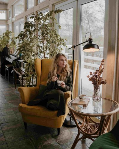 Femme assise dans un fauteuil jaune avec une tasse, ambiance cosy et chaleureuse, invitant à découvrir l’univers de Brigitte à travers son infolettre.
