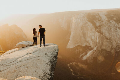 couple standing on the edge of a cliff at sunset
