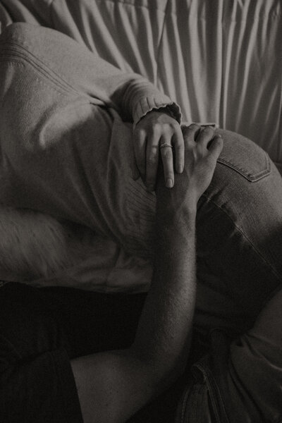 Couple holding hands while laying in bed for their in-home session.