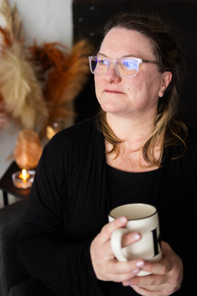 Katie holds a mug and wears glasses.