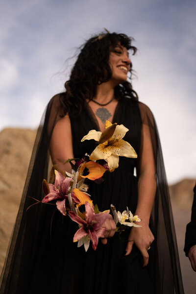 A bride in a black dress standing confidently at Artist's Palette, surrounded by the stunning, colorful hills of Death Valley, as her partner looks on.