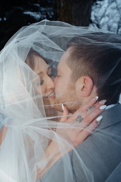 Winter wedding trendy flash image of the couple kissing under the veil, in Stettler Alberta