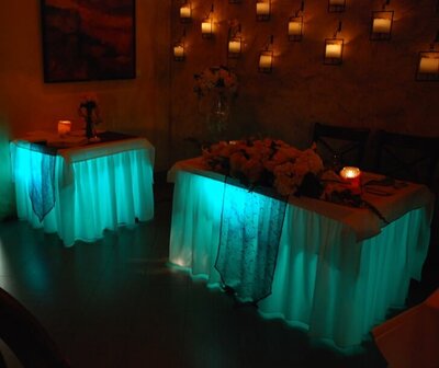 Dream of a white skirted table that is up lit internally so the white skirt glows in the reduced ambient lighting of the event with brilliant cyans, purples, ambers, reds, blues, and greens.