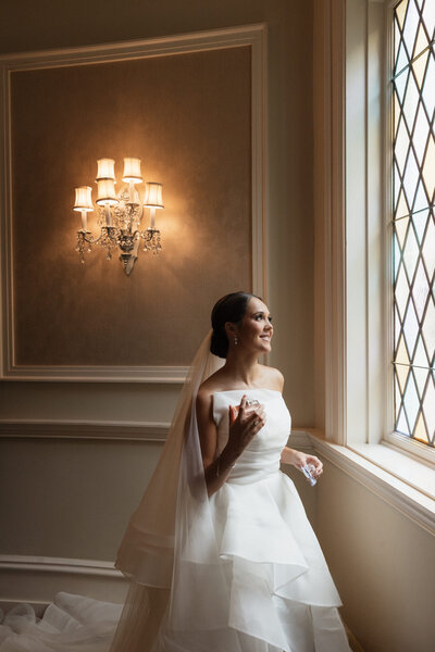Bride putting on her perfume as she looks out the window on her wedding day.