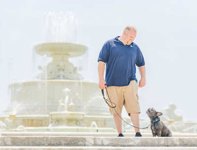 Matthew Lamarand smiling at a grey French bulldog in front of the Belle Isle fountain during a day training trip