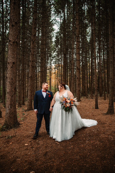 bride and groom laugh together while holding hands with tall pine trees surrounding them