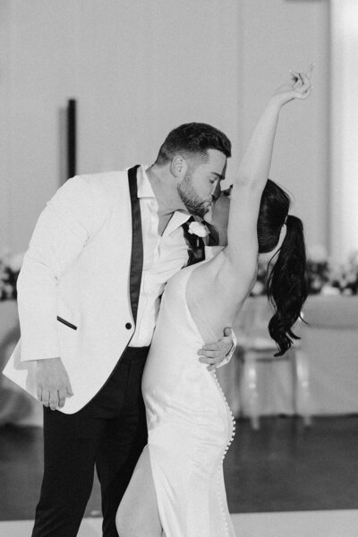 Black and white photo of bride kissing groom with her arm in the air