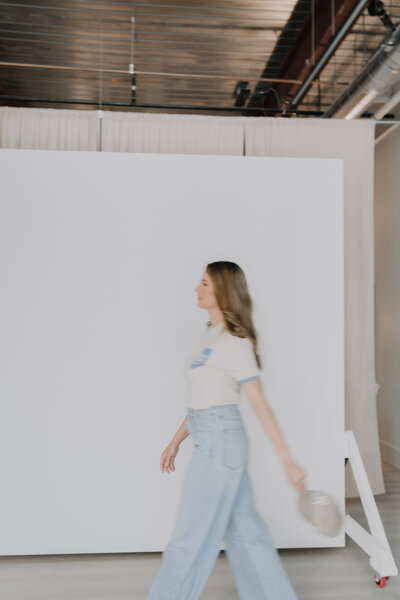 Megan Evans in jeans and a tee walking in front of a studio backdrop