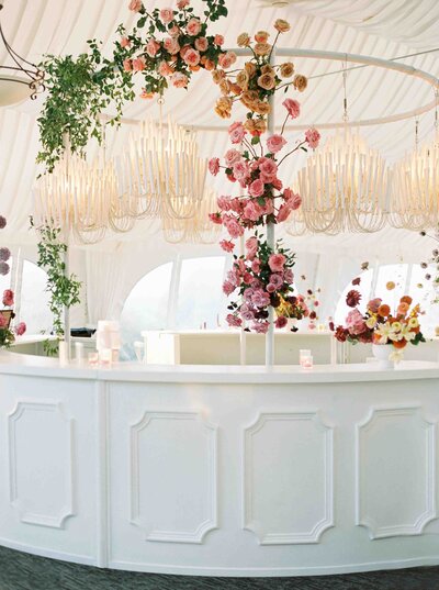 colorful floral instalation hanging over white custom wedding bar in a tent