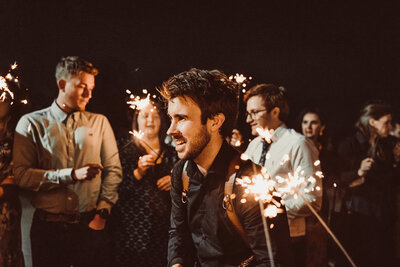 Tom Keenan smiling whilst getting ready for the bride and groom to walk through a tunnel of sparklers