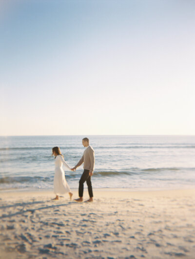 Couple holding hands walking along the beach with the ocean behind them