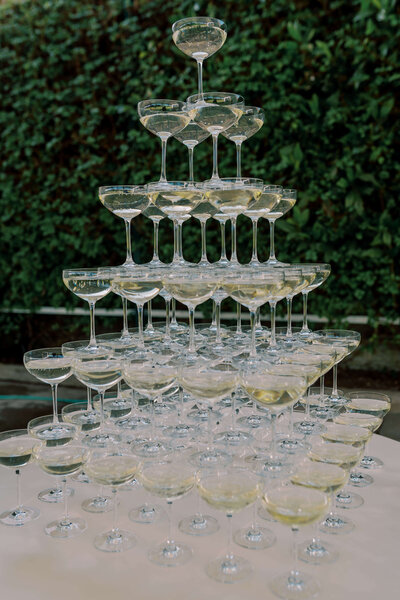 6 tier champagne tower displayed on a white table with a green leafy backdrop for a luxury party