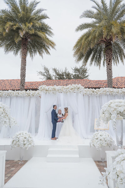 Bride and groom wedding ceremony with white draping and palm trees