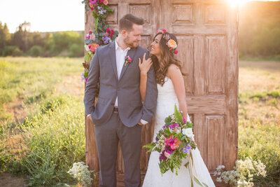 Bride and Groom pose together in front of a door placed in the middle of an open field