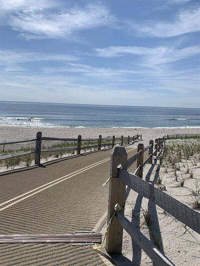 A simple wooden fence made of vertical planks, standing in a grassy area under a clear blue sky.