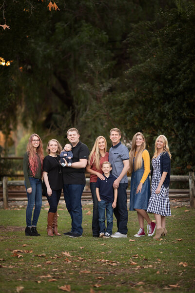 A joyful family captured by a Dallas family photographer in a natural outdoor setting, with everyone smiling and dressed casually in coordinated outfits.