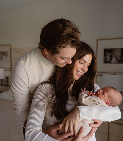 A new family. Dad and mom holding new born looking down on their baby. 