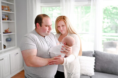 Mom and dad holding newborn baby in living room during lifestyle newborn portrait session.