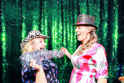 2 ladies posing against a green sequins backdrop, for a private  party entertainment using the Selfie pod party photo booth