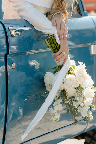 Bride holding a white bouquet while leaning against a vintage blue car during a Charleston elopement.