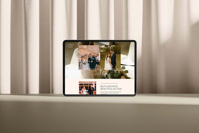 A tablet displaying a wedding planning website is placed on a light-colored surface. The screen shows a newlywed couple, a group photo, and text about event planning crafted with website design services for small business. Curtains are in the background.