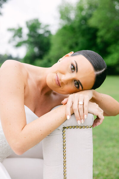 Bride resting her head on her hands as she leans sideways on a couch fr a portrait