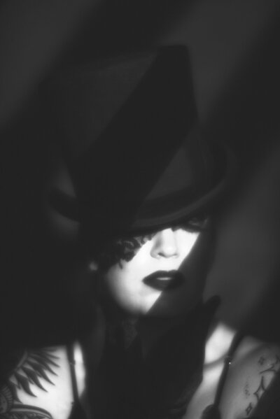 A black and white old hollywood glam image of a woman in a top hat and lace mask with blinds GOBO.