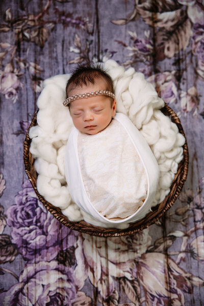 A newborn baby sleeps in a wooden bowl in a blue swaddle
