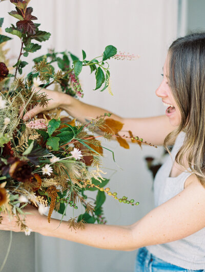 Woman smiling while arranging florals and greenery in a studio