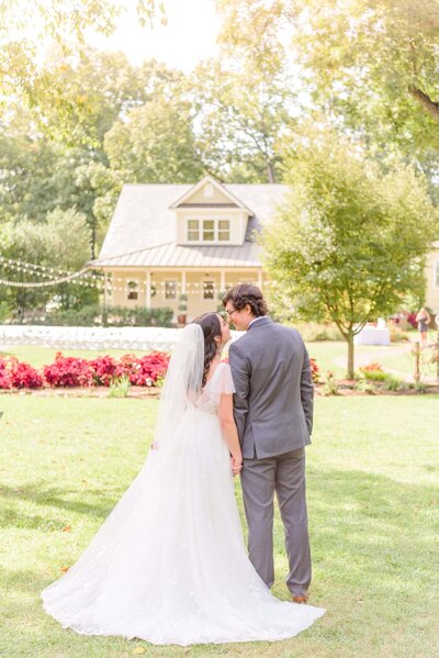 A bride and groom face away from the camera, and the Alexander Homestead house can be seen in the background.
