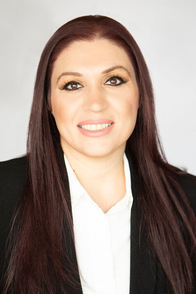 Headshot of a woman with long brown hair and brown eyes wearing a black blazer and white blouse.