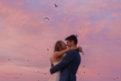 couple embrace with sunset clouds and birds in the background 