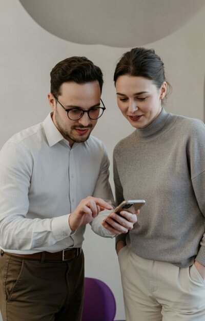 Couple standing close together and looking at a phone with gentle smiles, symbolizing teamwork, support, and readiness to begin the healing journey through Relationship Experts’ couples therapy and infidelity recovery services in Florida, US, UK, and Canada.