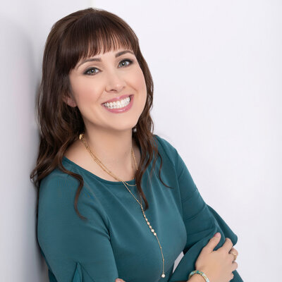 Headshot of Customer Experience keynote speaker and author, Brittany Hodak. She wears a teal dress and is standing against a wall.