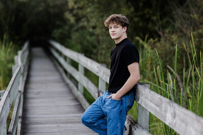 Young man  leaning against a railing at a park smiling.