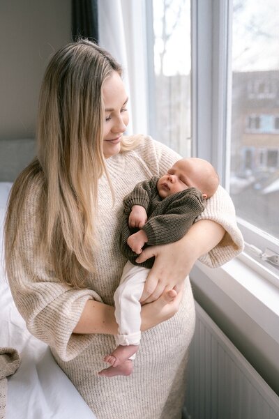 Moeder kijkt liefdevol naar haar zoontje die in haar armen ligt te slapen